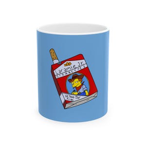 May include: A white ceramic mug with a light blue exterior. The mug features a cartoon illustration of a cigarette pack labeled "Laramie Jr. Cigarettes" with a cowboy character. The text "Ultra-Tar Kings" is also visible.