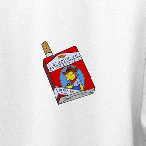 Op de afbeelding: Een rood en wit pakje "Laramie Jr. Cigarettes" met een cartoon cowboy illustratie. Op het pakje staat "ULTRA-TAR Kings" en er steekt een aangestoken sigaret uit.