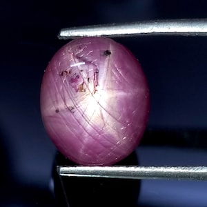 May include: A pink star ruby cabochon gemstone with a six-rayed star.