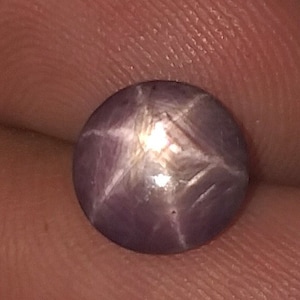 Puede incluir: Una piedra preciosa de zafiro estrellado púrpura con una estrella de seis puntas.