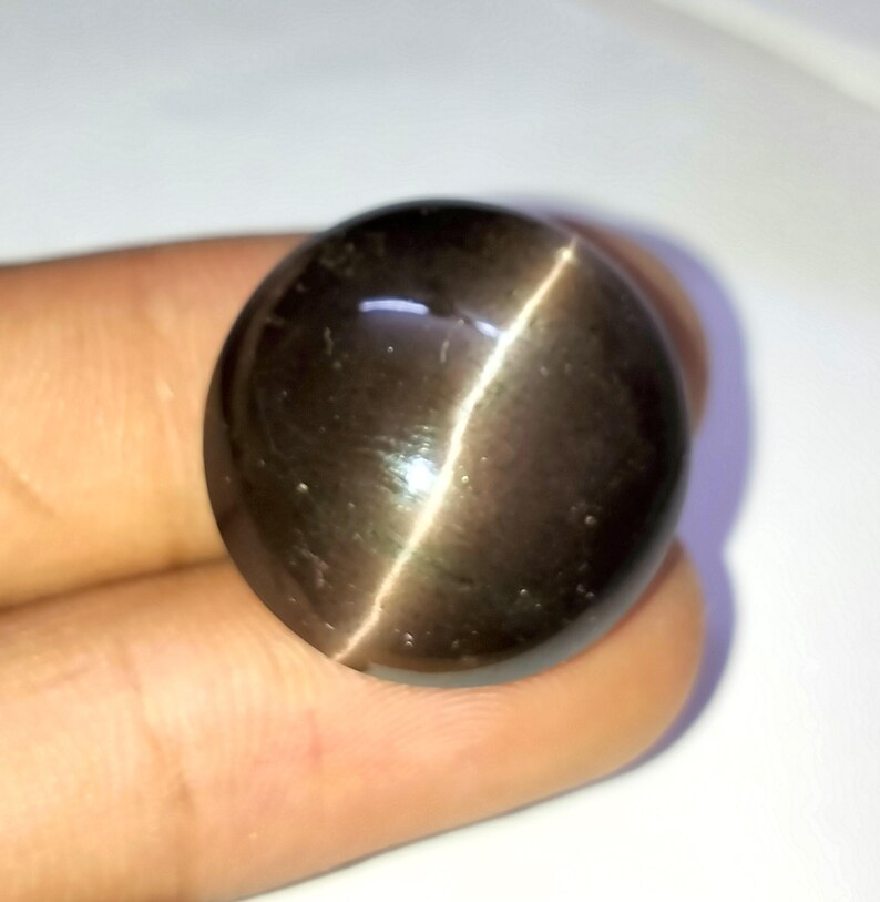 May include: A round, dark brown gemstone with a chatoyant effect, also known as a cat's eye gemstone.