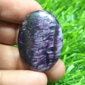 Peut inclure: Une pierre précieuse ovale en cabochon avec un motif strié de couleur violet et blanc. La pierre est polie et a une finition brillante.