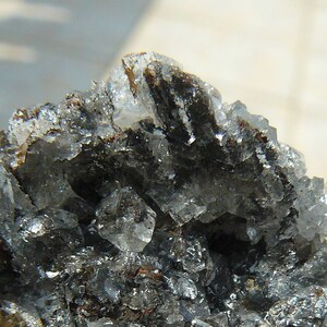 Op de afbeelding: Close-up van een mineraalmonster met een mix van kleuren. De steen heeft een donkere, mogelijk metalen kern, omgeven door doorschijnende, kristallijne structuren. De buitenste randen vertonen een roestbruine tint.