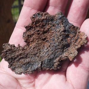 Könnte beinhalten: Nahaufnahme eines dunkelbraunen und schwarzen Metallstücks mit einer rauen, strukturierten Oberfläche. Das Metall scheint verrostet oder korrodiert zu sein.