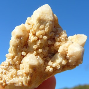 May include: A cluster of light brown crystals with a rough, textured surface. The crystals are arranged in a pointed, irregular shape.