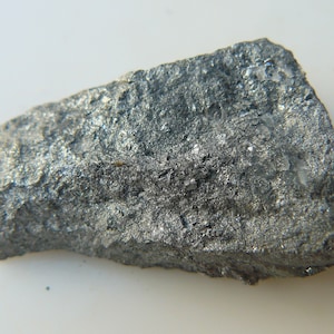 Può includere: Primo piano di una roccia metallica grigia e ruvida con un leggero bagliore iridescente.
