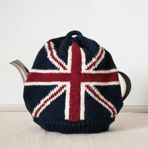 Può includere: Una coperta per teiera in maglia blu navy con il design della bandiera britannica in rosso e bianco. Copre una teiera d'argento, aggiungendo un tocco decorativo e patriottico.