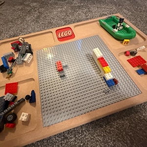 May include: A wooden LEGO play tray with a gray baseplate and several compartments. The tray features a red LEGO logo and contains various LEGO bricks, a green boat, and a LEGO figure.