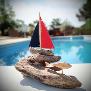 Barco velero en madera a la deriva, hecho a mano, rodeado de tres peces. Pieza única.