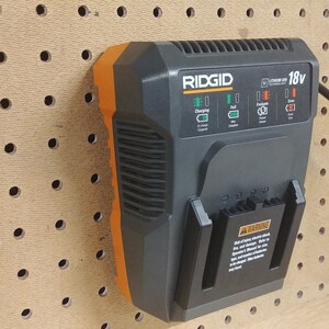 May include: A black and orange RIDGID 18v Lithium-Ion battery charger with a black power cord plugged in. The charger is mounted on a pegboard.