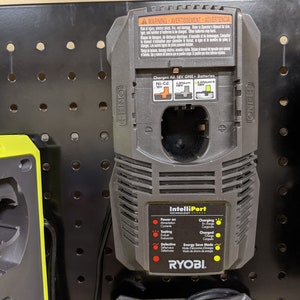 May include: A black and gray Ryobi battery charger with the text "IntelliPort Technology" and a diagram showing the different battery types it can charge. The charger has a warning label in English, French, and Spanish.