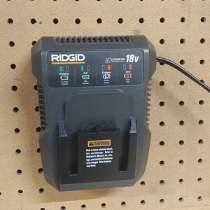 May include: A black Ridgid 18v battery charger with a green and orange display. The charger is plugged in and has a black cord.