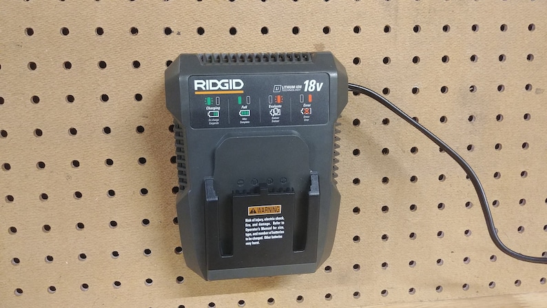 May include: A black Ridgid 18v battery charger with a green and orange display. The charger is plugged in and has a black cord.