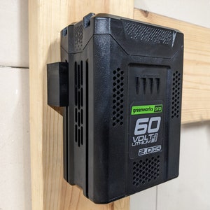 May include: A black battery pack with a green and white label that reads "greenworks pro 60 VOLT MAX LITHIUM 2.0 HC". The battery pack is mounted on a wooden wall.