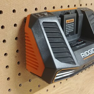 May include: A black and orange Ridgid battery charger with a warning label and a power cord. The charger is mounted on a pegboard.
