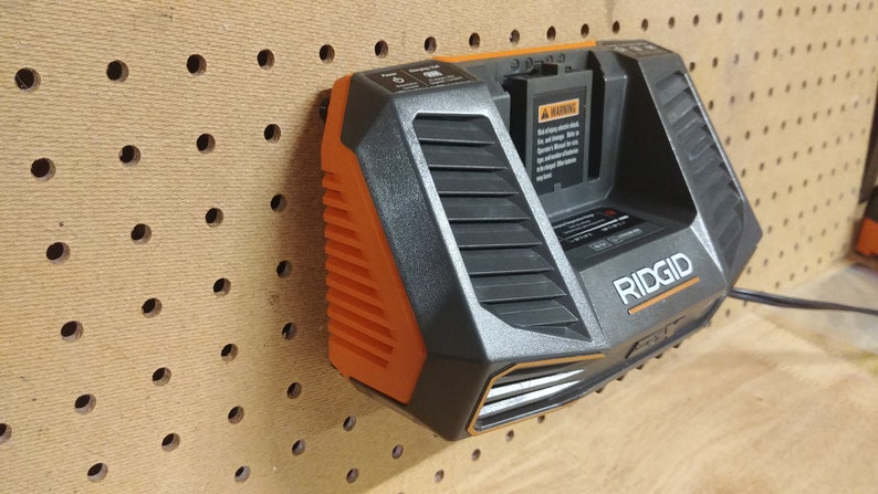 May include: A black and orange Ridgid battery charger with a warning label and a power cord. The charger is mounted on a pegboard.