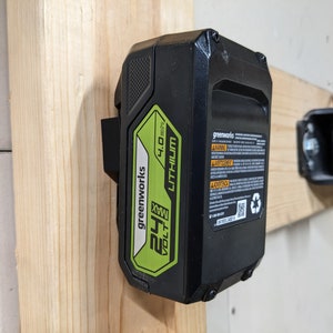 May include: A black and green 24 volt MAX lithium-ion battery for power tools. The battery is labeled "Greenworks" and has a warning label.