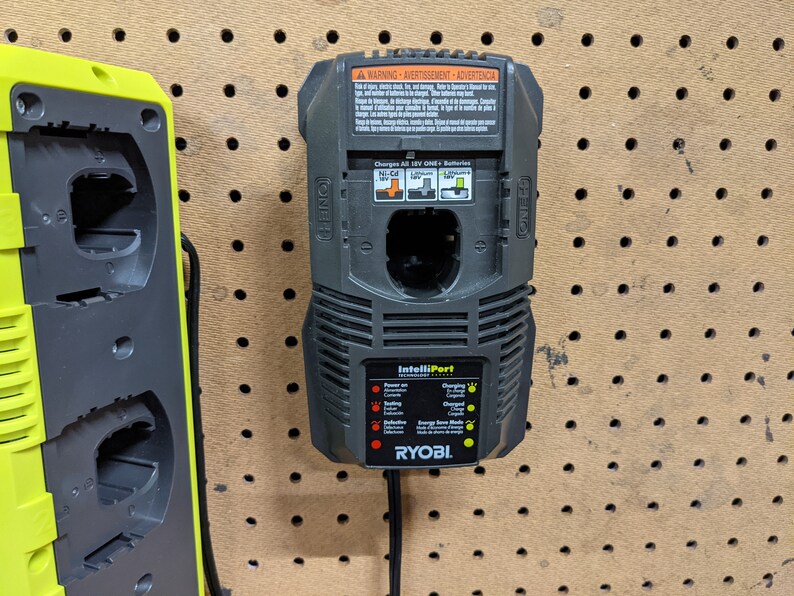 May include: A black Ryobi IntelliPort charger with a yellow indicator light. The charger is mounted on a pegboard wall and has a warning label with text in English, French, and Spanish.