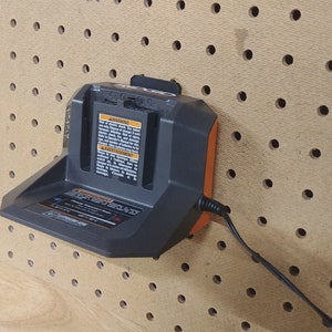 May include: A black and orange battery charger with a power cord plugged in. The charger is mounted on a pegboard wall.