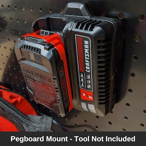 May include: A black and red Craftsman pegboard mount for a 12/20 volt lithium-ion battery. The mount has a slot for the battery and a hook for hanging on a pegboard.