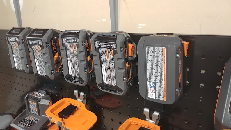 May include: A row of six black and orange power tool batteries hanging on a pegboard wall. The batteries are labeled "20V MAX*" and have a warning label on the side.
