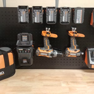 May include: A black pegboard with a variety of Ridgid power tools, including two drills, multiple batteries, and two chargers. A black and orange tool bag is in the foreground.