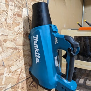 May include: A blue and black Makita 18V cordless blower. The blower has a black nozzle and a blue handle with a black grip. The Makita logo is printed in white on the side of the blower.