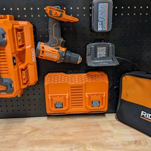 May include: An assortment of orange and black RIDGID power tools and accessories, including a drill, battery chargers, and batteries, mounted on a black pegboard. A black bag with the RIDGID logo is also present.