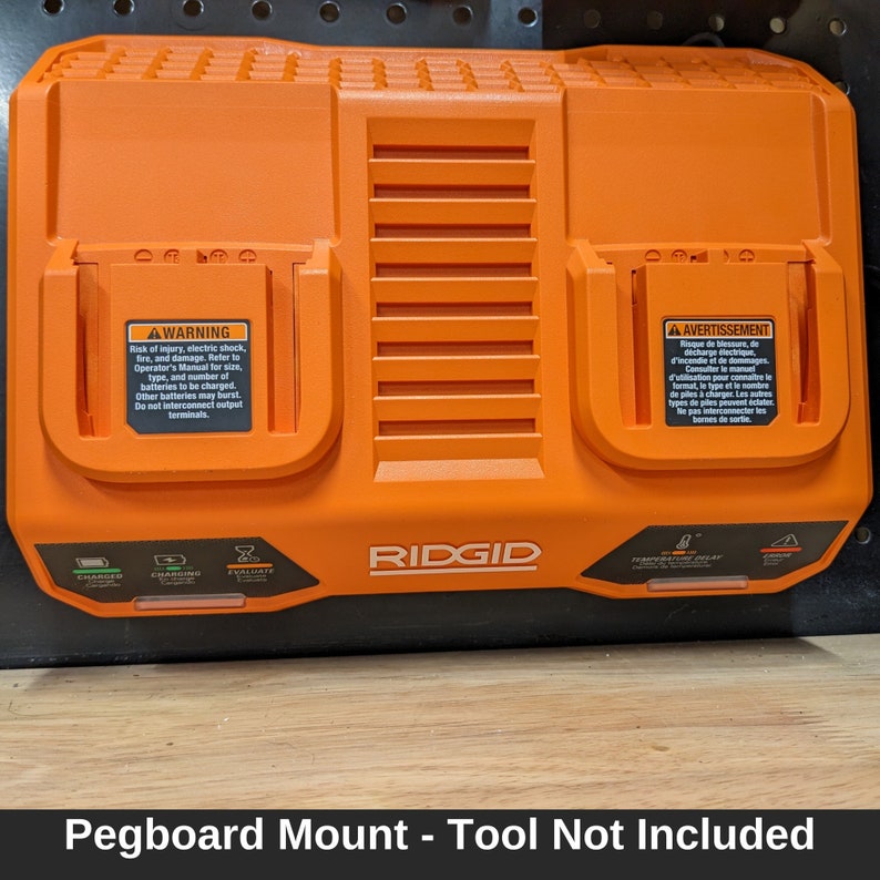May include: An orange RIDGID battery charger with two charging bays. The charger has warning labels and indicator lights for charging status and temperature delay. The text "Pegboard Mount - Tool Not Included" is at the bottom.