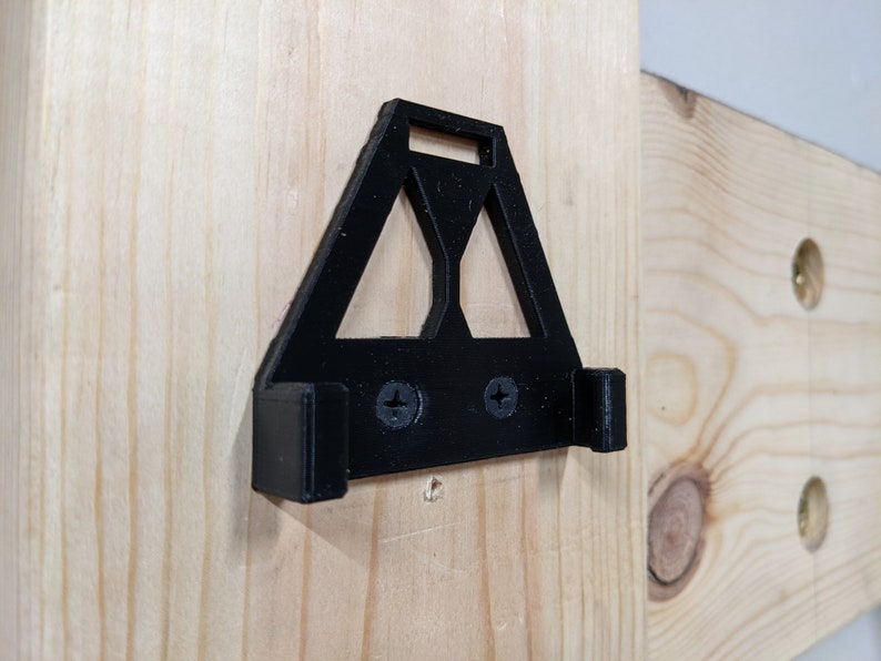 May include: A black plastic wall mount with two screws. The mount has a triangular shape with a cutout in the centre.