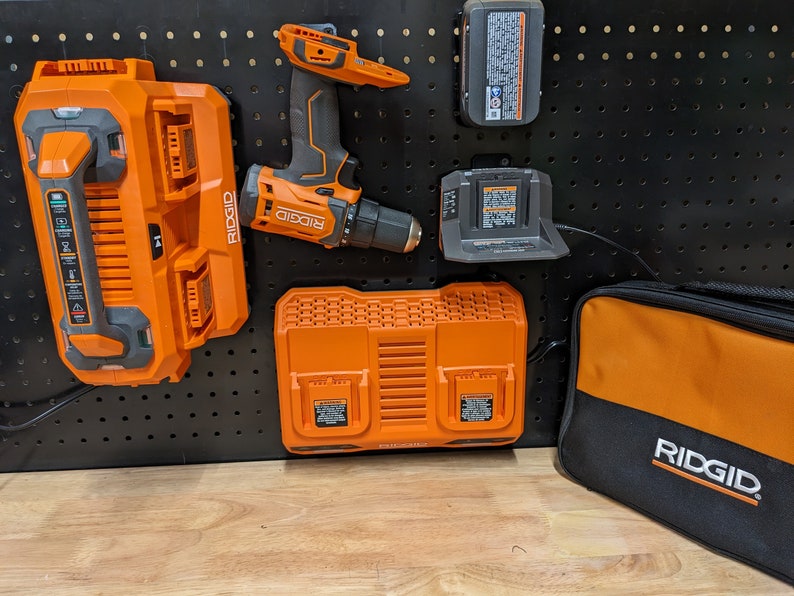 May include: A set of orange and black Ridgid power tools, including a drill, two batteries, a charger, and a carrying case. The tools are hanging on a pegboard.