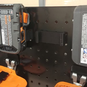 May include: A black pegboard with multiple orange and black battery packs hanging on it. The battery packs are labeled "2Ah" and "4Ah".