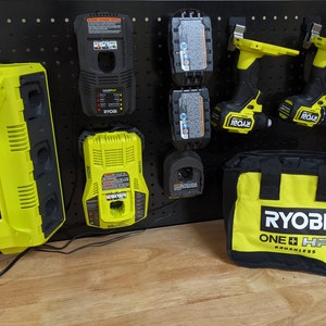May include: A black pegboard with a variety of Ryobi tools, including two cordless drills, a dual battery charger, a single battery charger, and four batteries. The tools are all yellow and black and have the Ryobi logo on them. There is also a black and yellow Ryobi tool bag with the text "Ryobi One+ HP Brushless" on it.
