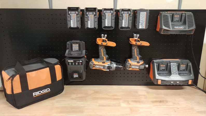 Puede incluir: Una colecci&oacute;n de herramientas el&eacute;ctricas y accesorios, incluyendo taladros, cargadores y bater&iacute;as, exhibidos en una panel perforado negro. Las herramientas son principalmente grises y naranjas, con la marca "RIDGID" visible en varios art&iacute;culos. Tambi&eacute;n hay una bolsa de herramientas negra y naranja.