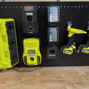 May include: A black pegboard with a yellow Ryobi multi-charger, two yellow Ryobi batteries, two yellow Ryobi drill drivers, and a yellow Ryobi single charger.