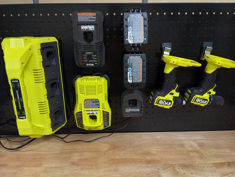 May include: A black pegboard with a yellow Ryobi multi-charger, two yellow Ryobi batteries, two yellow Ryobi drill drivers, and a yellow Ryobi single charger.