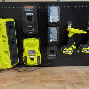 May include: A black pegboard with a yellow Ryobi multi-charger, two yellow Ryobi batteries, two yellow Ryobi drill drivers, and a yellow Ryobi single charger.