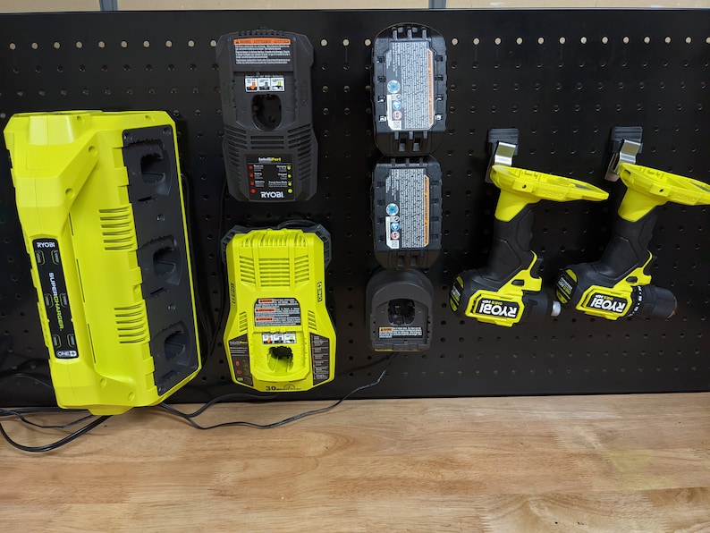 May include: A black pegboard with a yellow Ryobi multi-charger, two yellow Ryobi batteries, two yellow Ryobi drill drivers, and a yellow Ryobi single charger.