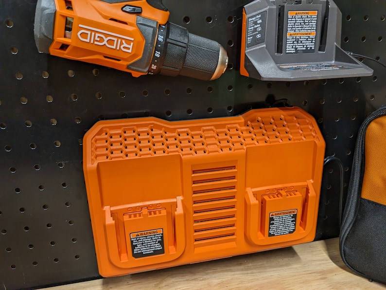 May include: Orange and black power tool accessories, including a drill, battery charger, and dual-bay battery charger. The drill is labeled "RIDGID". The battery charger has a warning label. The items are mounted on a black pegboard.