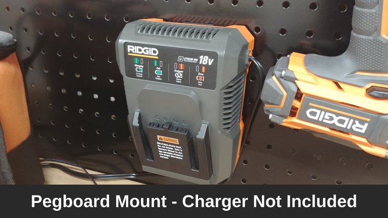 May include: A black and orange RIDGID 18V charger mounted on a pegboard. The charger has a green light indicating it is plugged in. The text "RIDGID 18V" is visible on the charger.