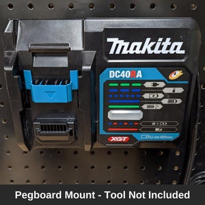 Puede incluir: Un cargador de batería Makita DC40RA 40Vmax XGT azul y negro con un soporte para tablero de clavijas. El cargador tiene una pantalla digital con luces verdes, azules y rojas.