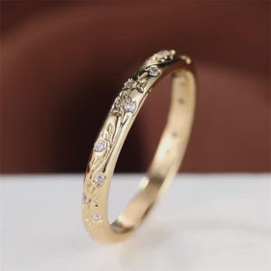 May include: A gold ring with an engraved floral pattern and small gemstones. The ring's design includes detailed flowers and leaves. The band has a polished finish, and the overall aesthetic is elegant and refined.