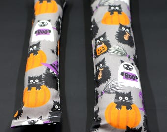 May include: Two gray catnip toys with a Halloween theme. The toys are shaped like long pillows and feature black cats, pumpkins, and ghosts. The larger toy is about 12 inches long and the smaller toy is about 8 inches long.