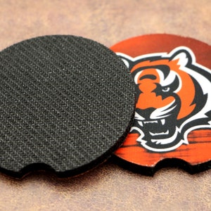 May include: A round, black, non-slip coaster with a printed design of an orange and black tiger on a wood-grain background. The tiger's face is visible, with a fierce expression.