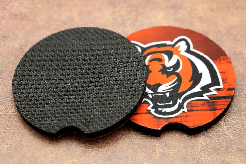 May include: A round, black, non-slip coaster with a printed design of an orange and black tiger on a wood-grain background. The tiger's face is visible, with a fierce expression.