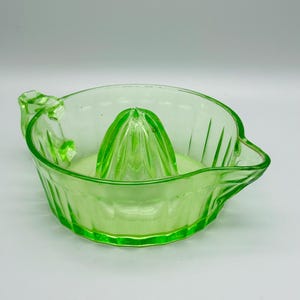 Peut inclure: Presse-agrumes vintage en verre vert clair. Il a une forme de bol avec un bec verseur et une poignée. Le centre présente un presse-agrumes rainuré pour extraire le jus. Le verre présente un motif nervuré à l'extérieur.