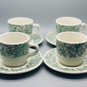 May include: Set of four white ceramic teacups and saucers with a green floral pattern.