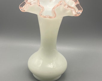 May include: A white milk glass vase with a ruffled pink rim. The vase has a round base and a tall, slender neck.