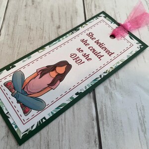 Puede incluir: Un marcap&aacute;ginas verde y blanco con un dise&ntilde;o floral. Presenta una ilustraci&oacute;n de dibujos animados de una persona sentada con el texto "She believed she could, so she DID!"