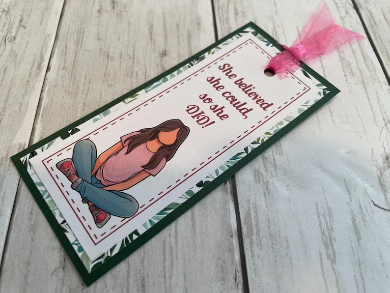 Puede incluir: Un marcap&aacute;ginas verde y blanco con un dise&ntilde;o floral. Presenta una ilustraci&oacute;n de dibujos animados de una persona sentada con el texto "She believed she could, so she DID!"
